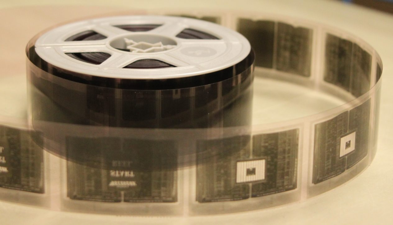 Rollo de microfilm desplegado, con los fotogramas de los documentos micrograbados visibles sobre la película